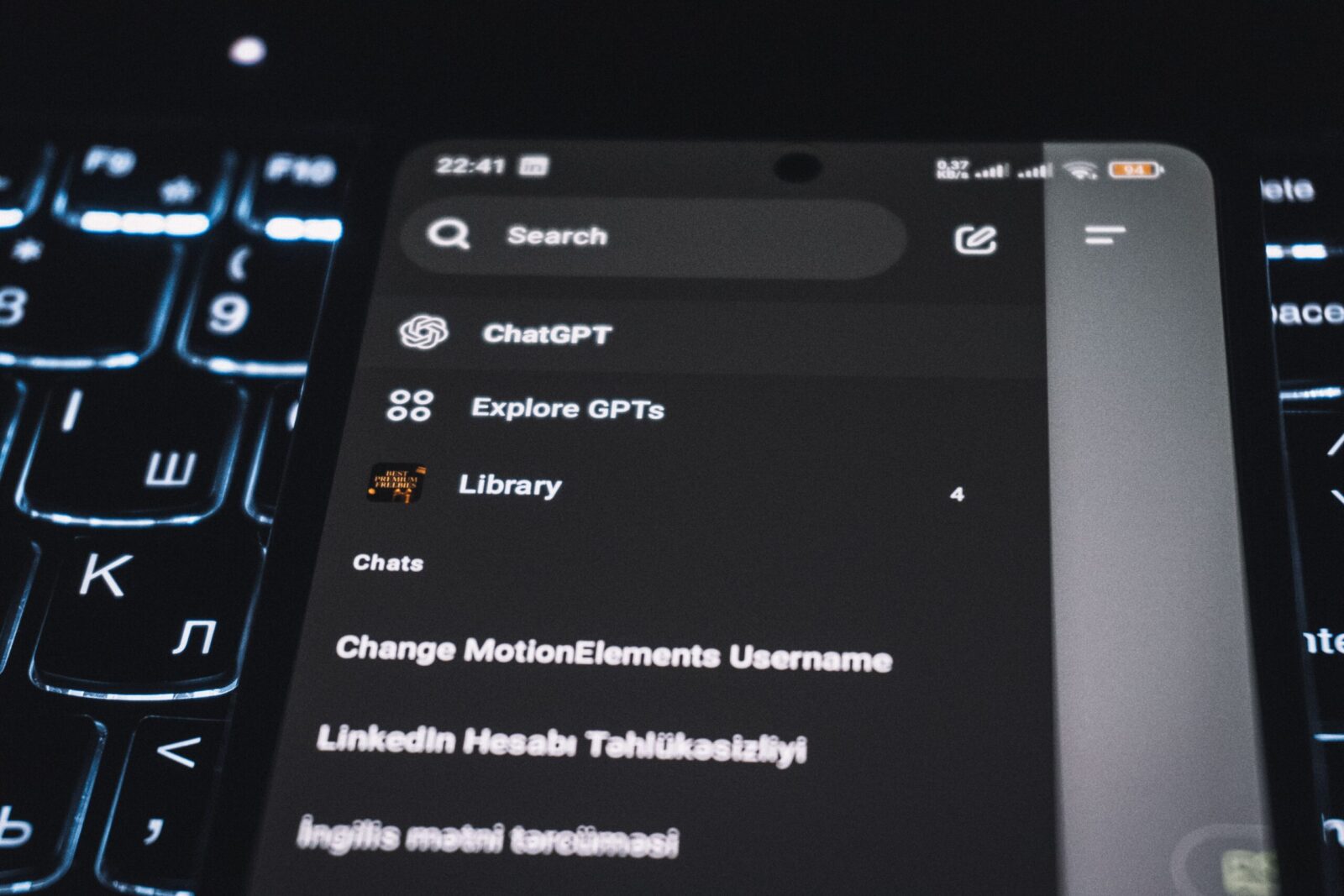 Close-up of a smartphone displaying a chat app interface with a backlit keyboard in the background.